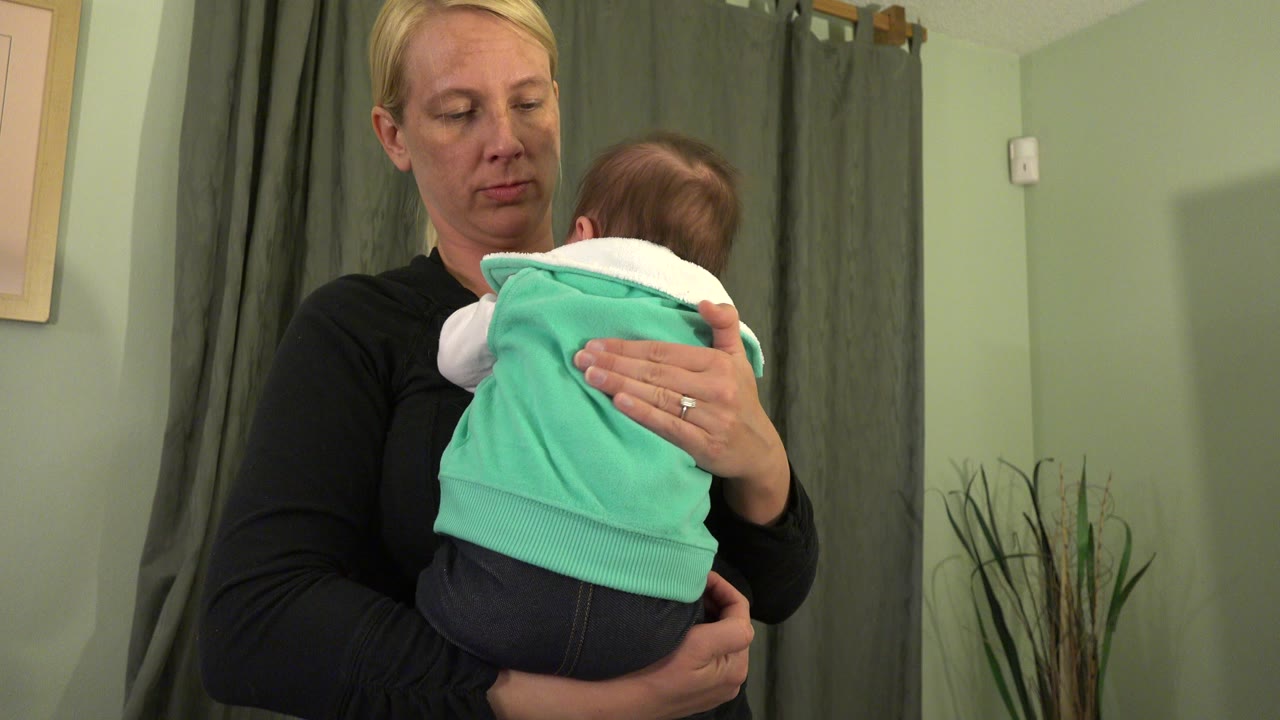 Woman holding a baby against her shoulder indoors.