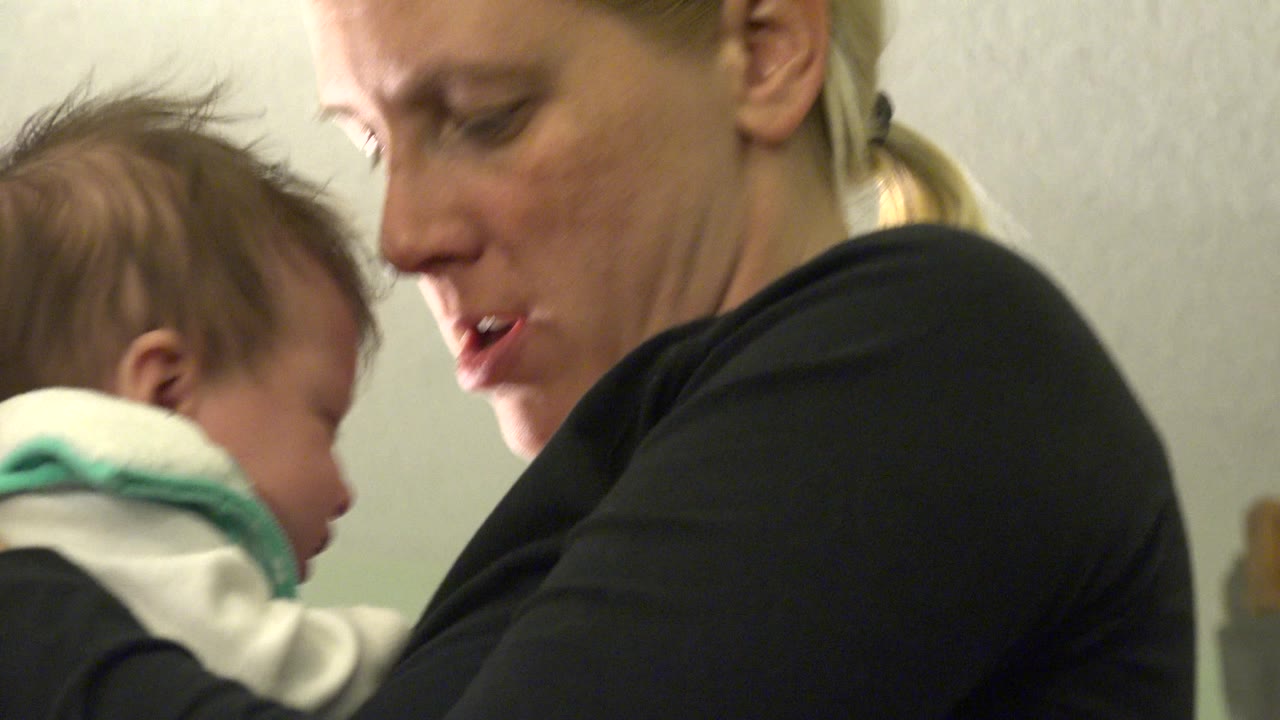 At 0:01, the baby faces the mother's shoulder while the mother looks down, keeping the frame tight on their faces and upper bodies.
