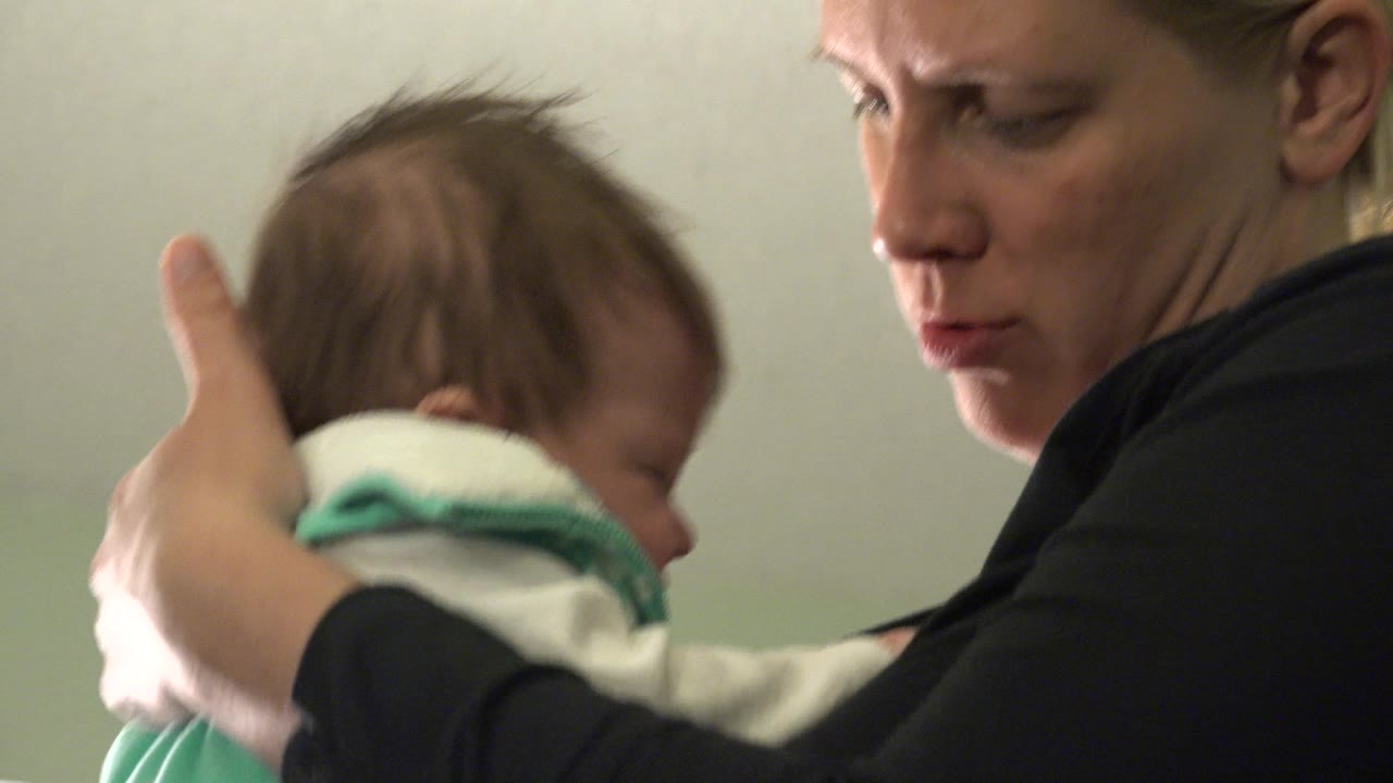 Woman supporting an infant with her hand in a tight indoor close-up.