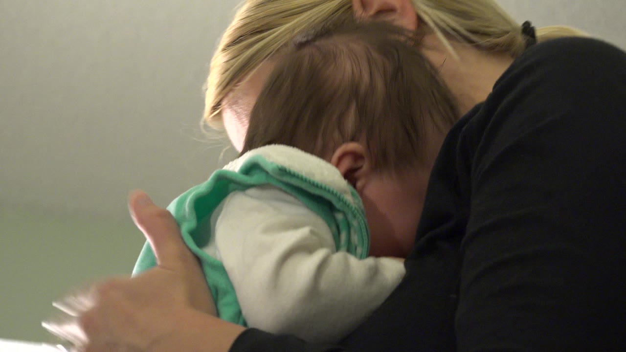 At 0:01, the baby leans into the woman while her hand supports the child's back in the tight indoor frame.
