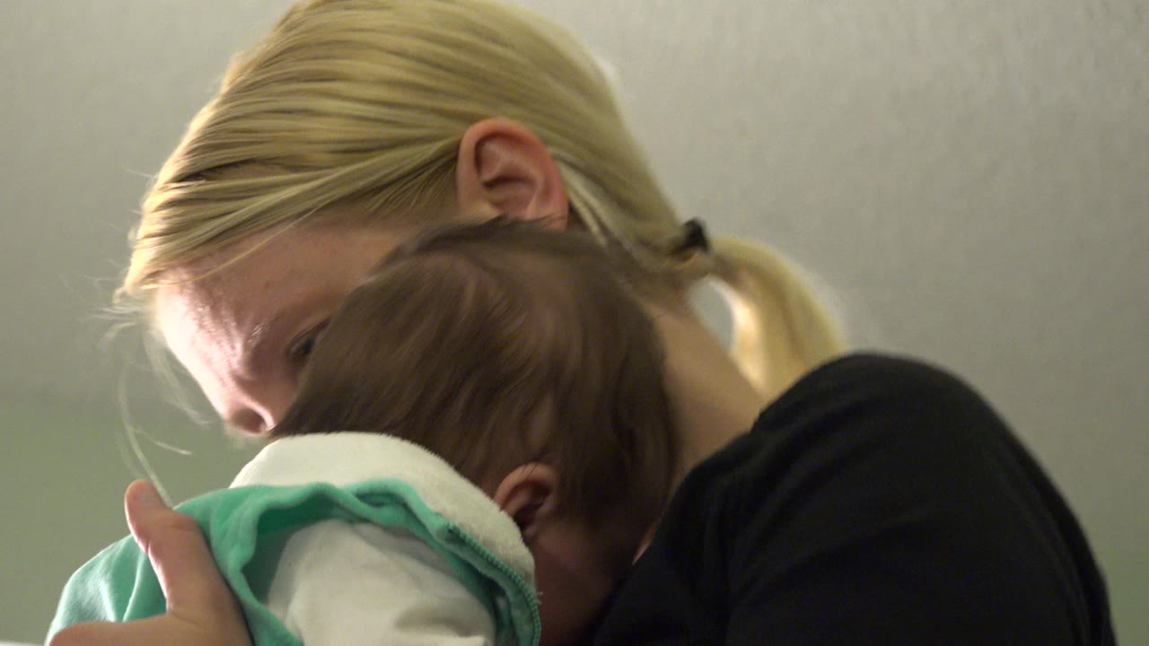 Woman looking down while cradling a baby in her arms.