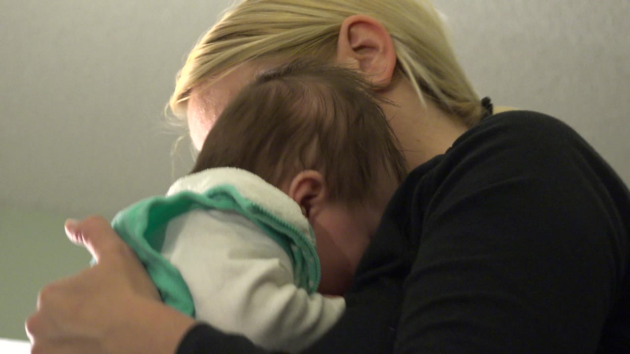 Blonde woman holding an infant close to her shoulder.