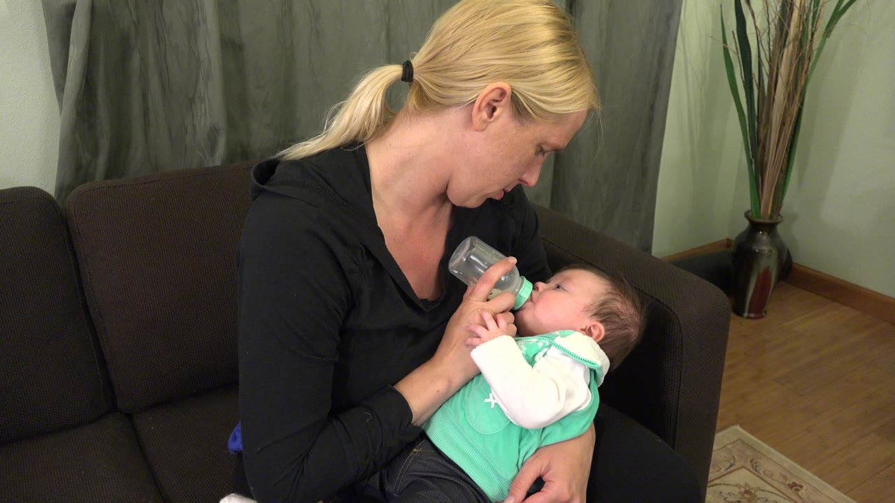 Mother holding infant during bottle feeding on couch.