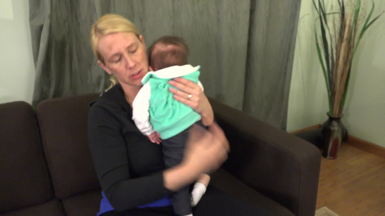Mother pats the baby while holding the child close on the couch.