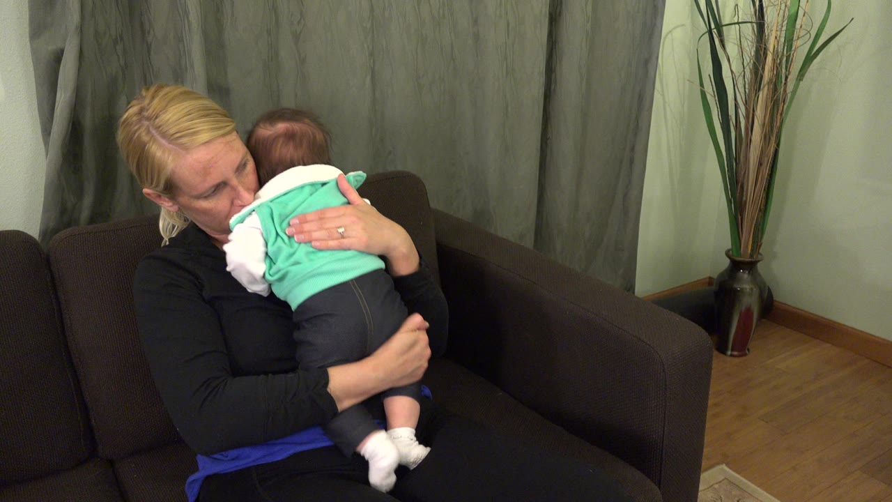 Woman holding a baby close while seated on a brown couch.