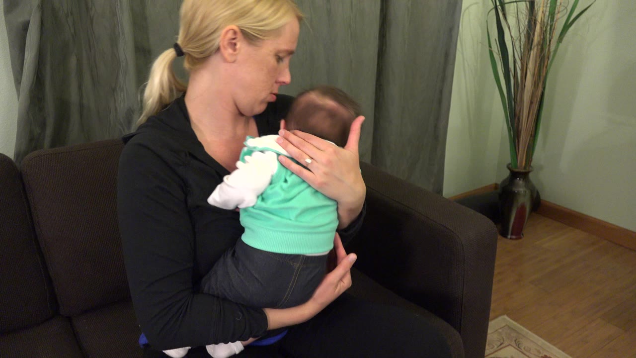 Mother holding a baby against her shoulder on a couch.