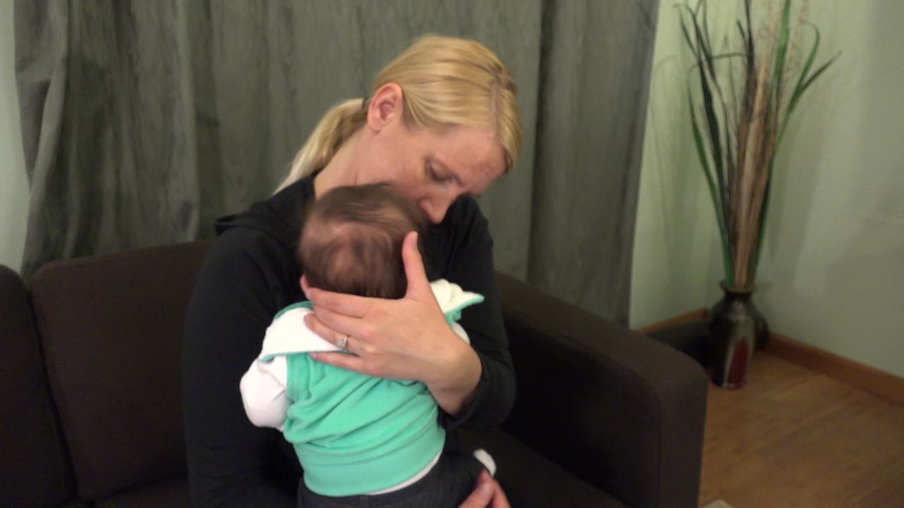 Mother holding an infant against her chest on a dark couch.