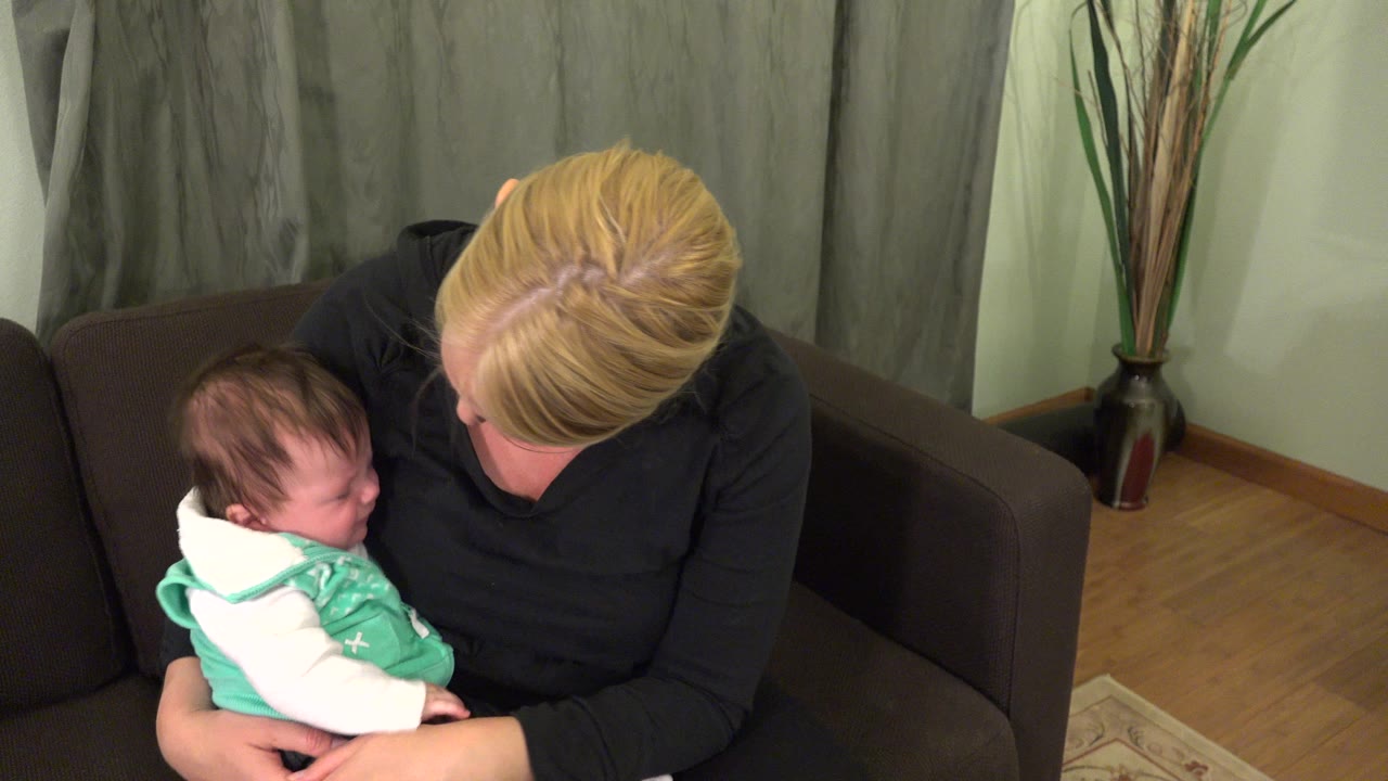Woman in a black shirt holding a baby on a brown sofa.