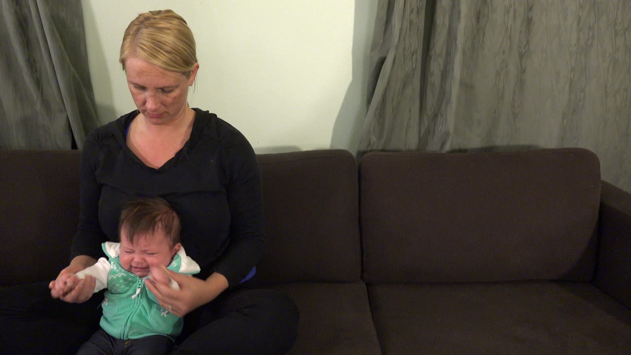 Woman seated on a sofa holding a crying baby.