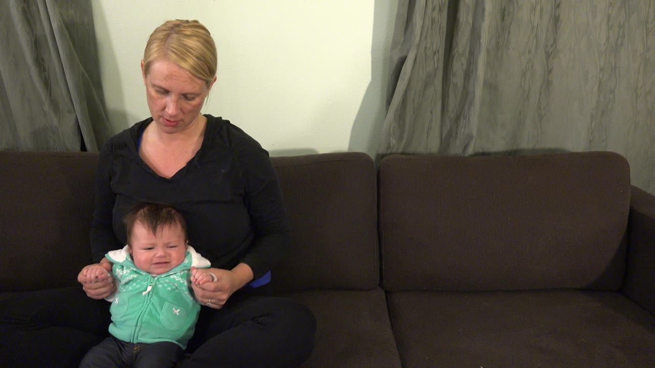 Baby crying while woman supports both arms.