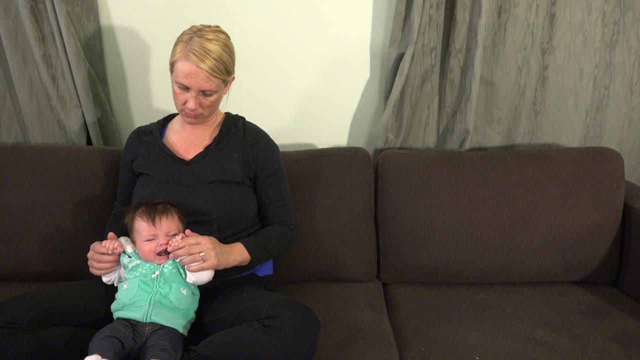 Baby crying while woman holds both hands.