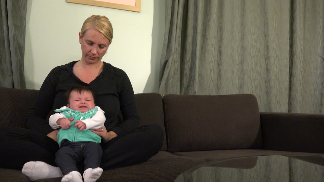 Woman seated on a dark couch holding a baby on her lap.