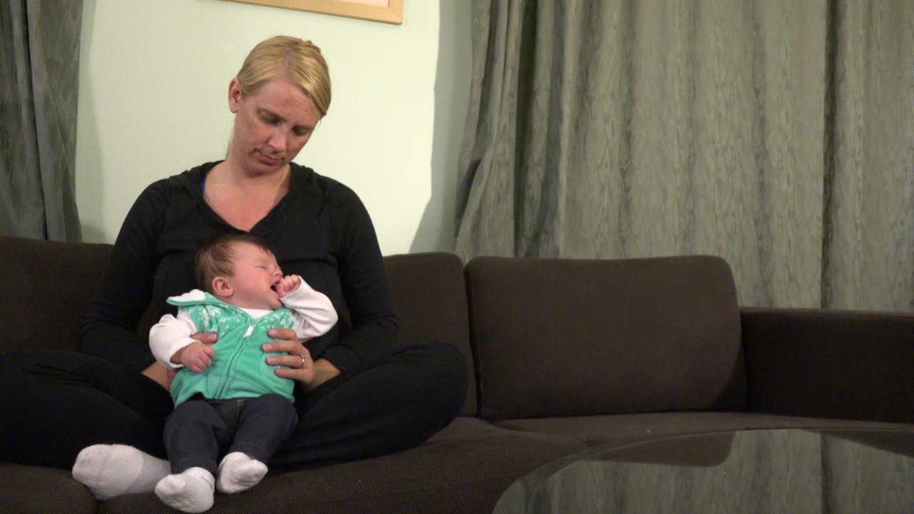 Mother sitting on a couch holding a baby on her lap.