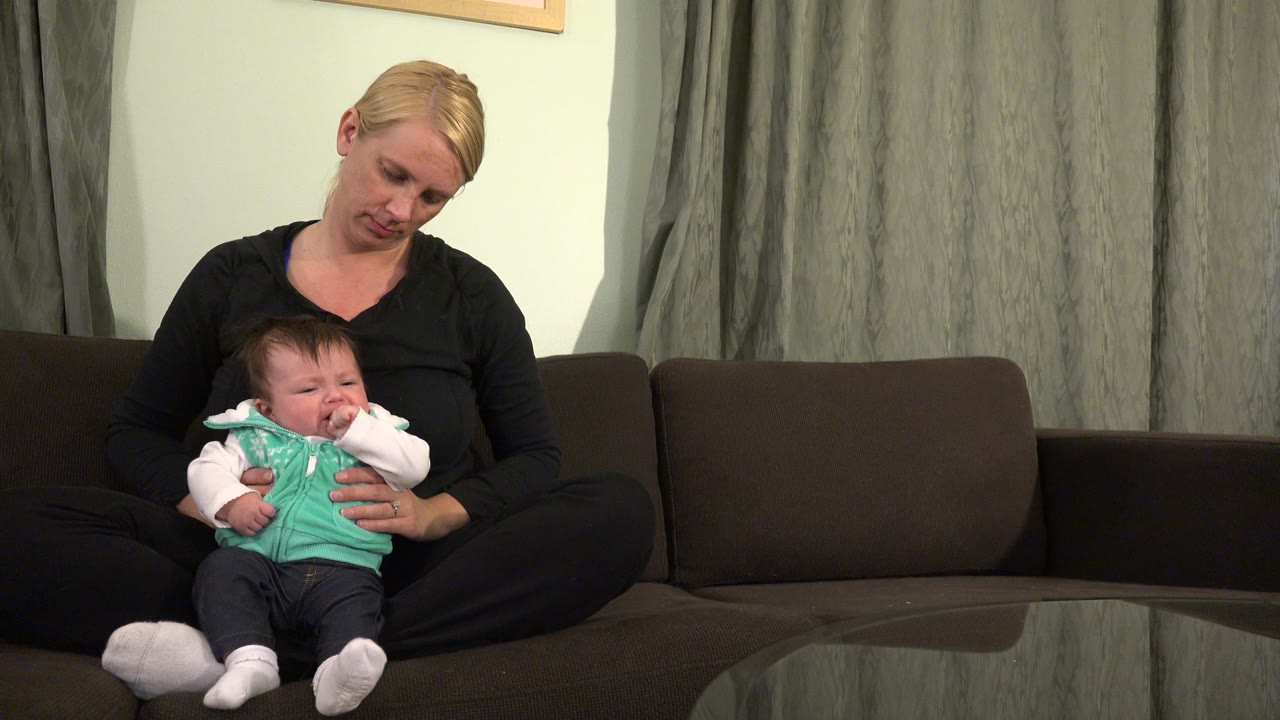 Baby raises a hand while seated on a woman's lap.