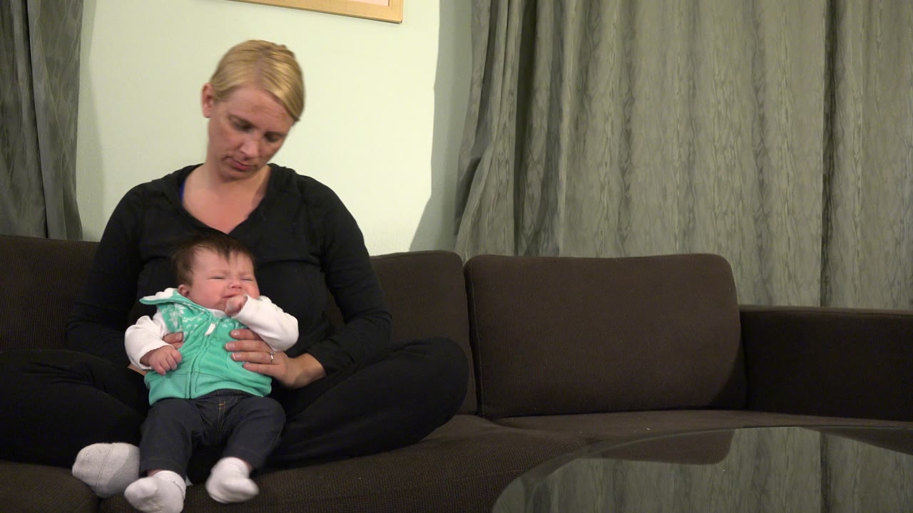 Mother seated on couch holding a crying baby in her lap.