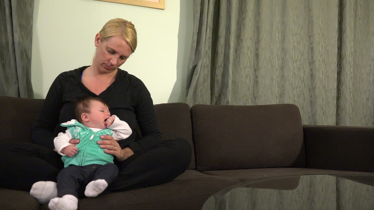 Mother sitting on a couch holding a baby in her lap.