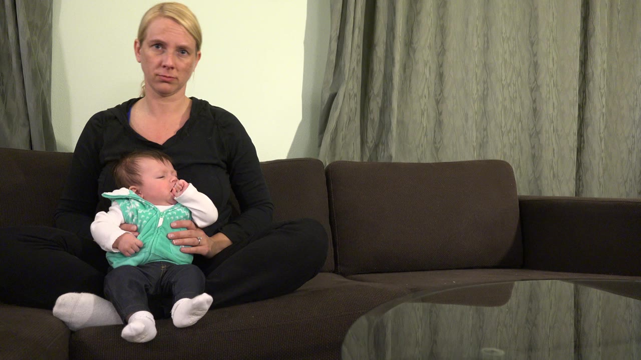 The Westminster home interior shows the woman seated upright as the baby leans against her chest with one hand near the face.