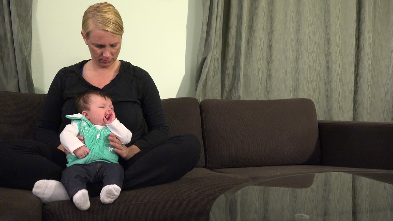 Mother holding a crying newborn on a dark couch.