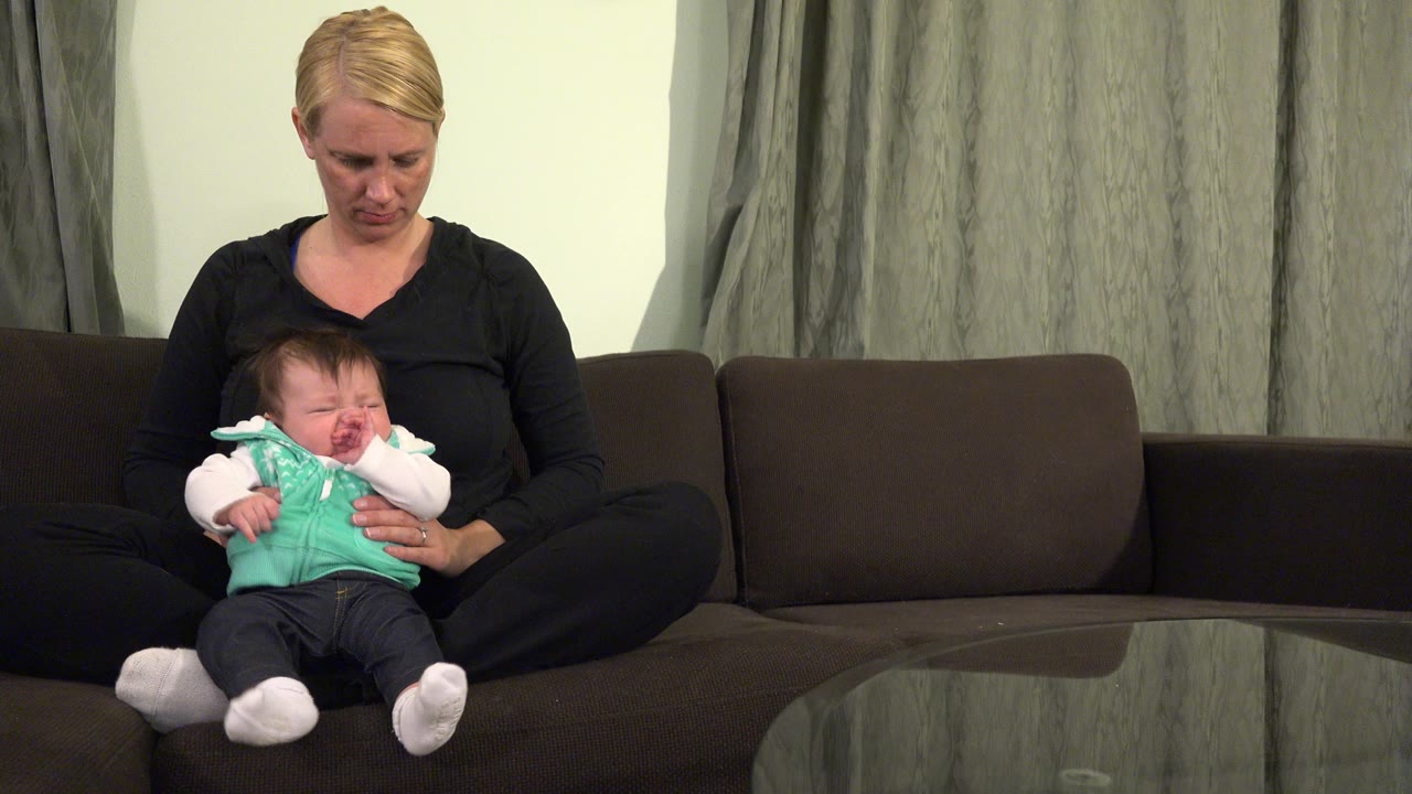 Blonde woman sitting cross-legged on a sofa holding a baby.