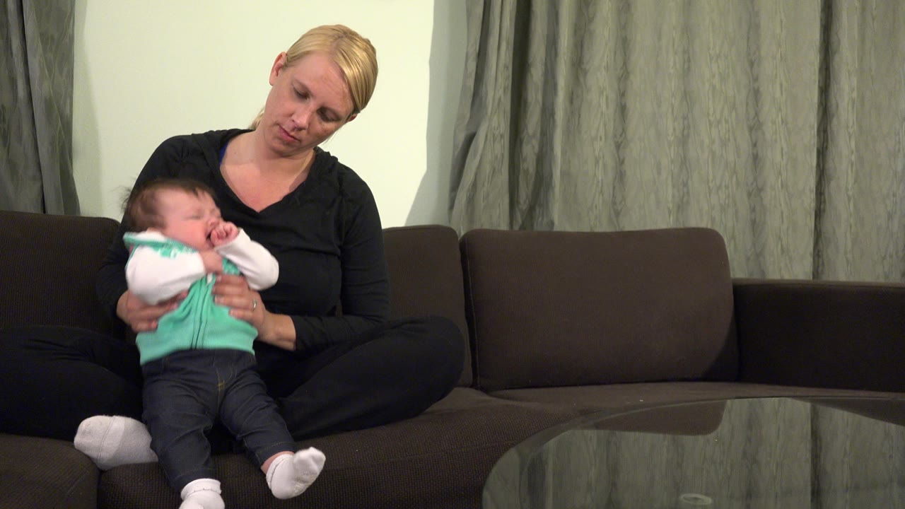 Woman holding a crying baby on a brown sofa.