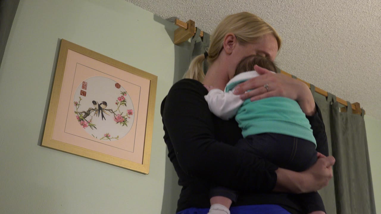 At 0:01 in Westminster, Colorado, the mother keeps the baby tucked against her shoulder while the low angle shows more of the ceiling and curtain rod behind them.