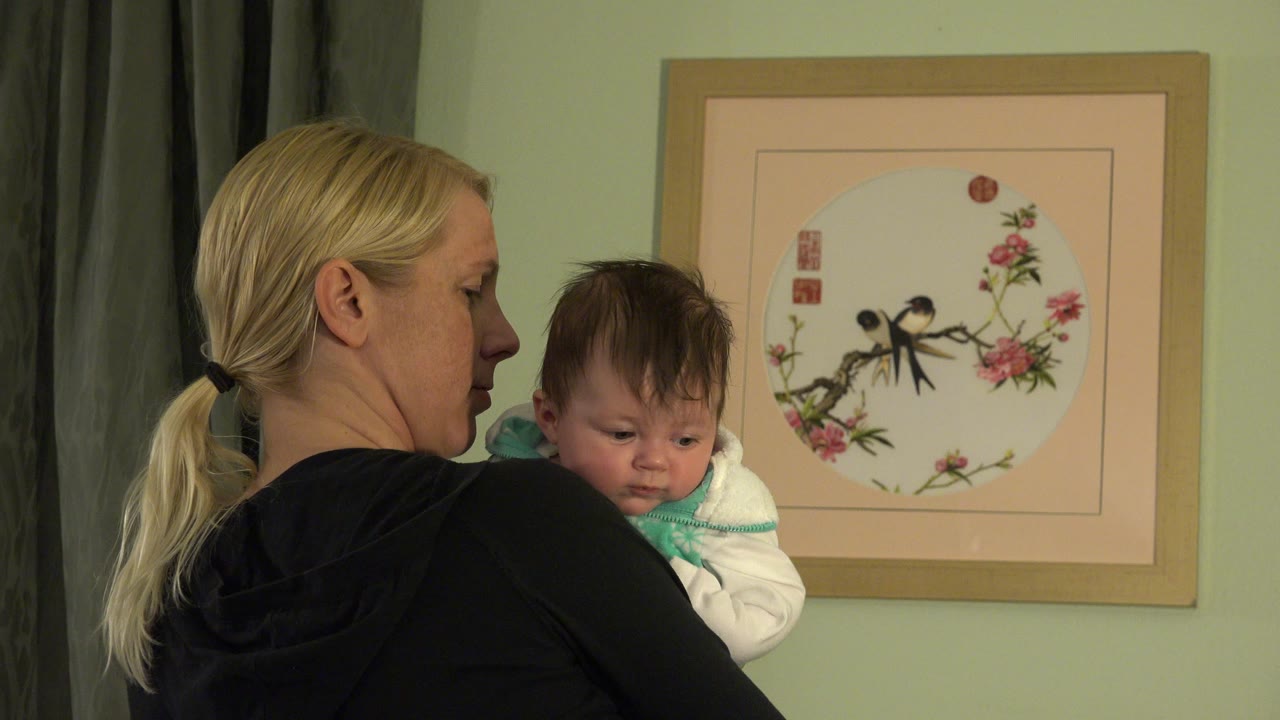 Blonde woman holding a baby near framed wall art.