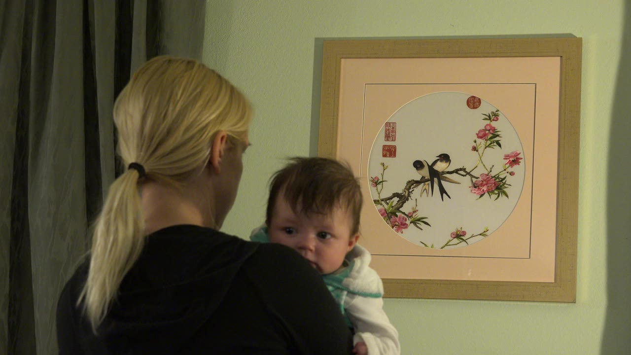 Woman holding a baby beside framed wall artwork