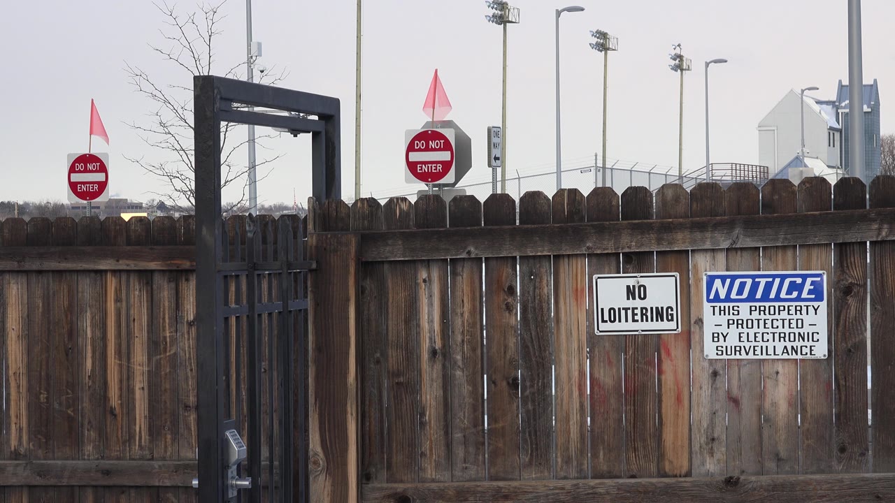 Opening frame of a Westminster, Colorado gated area with a black metal gate at left, red do-not-enter signs behind the fence, posted notices on the wooden boards, and no visible people.