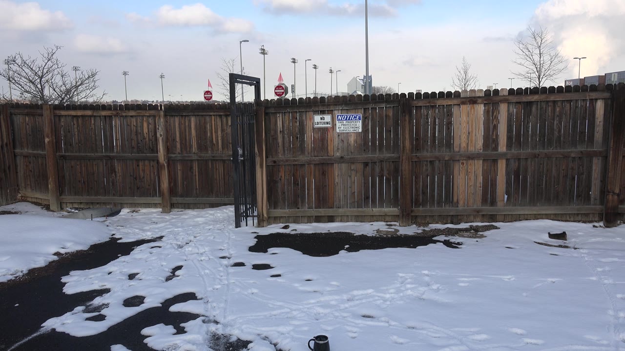 Black gate beside a weathered fence under clouds.