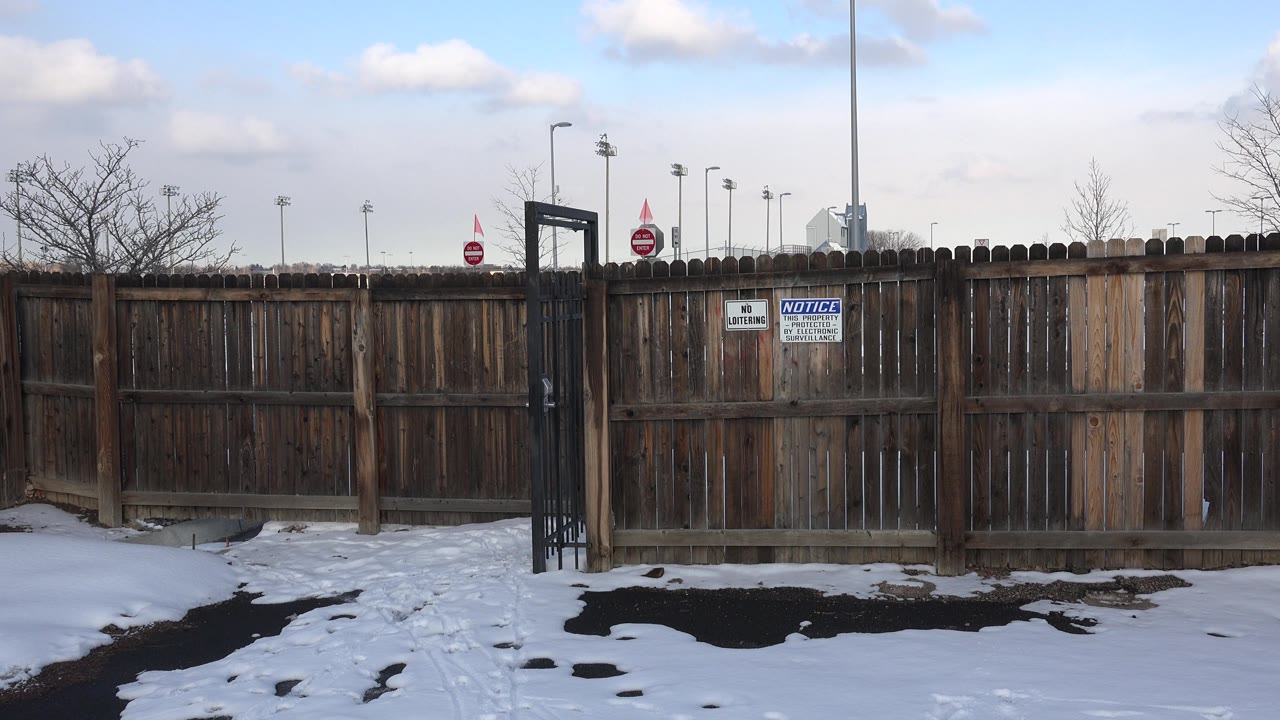 Fence line with posted signs, snow, and poles in background.