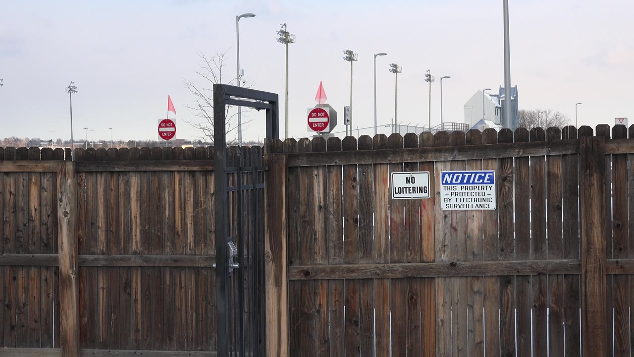 In Westminster, Colorado, a weathered brown wooden fence carries no loitering and electronic surveillance signs beside a black metal gate, with no visible people.