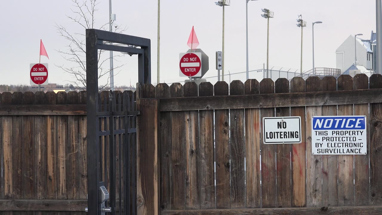 Weathered wooden fence with posted warning signs and black gate