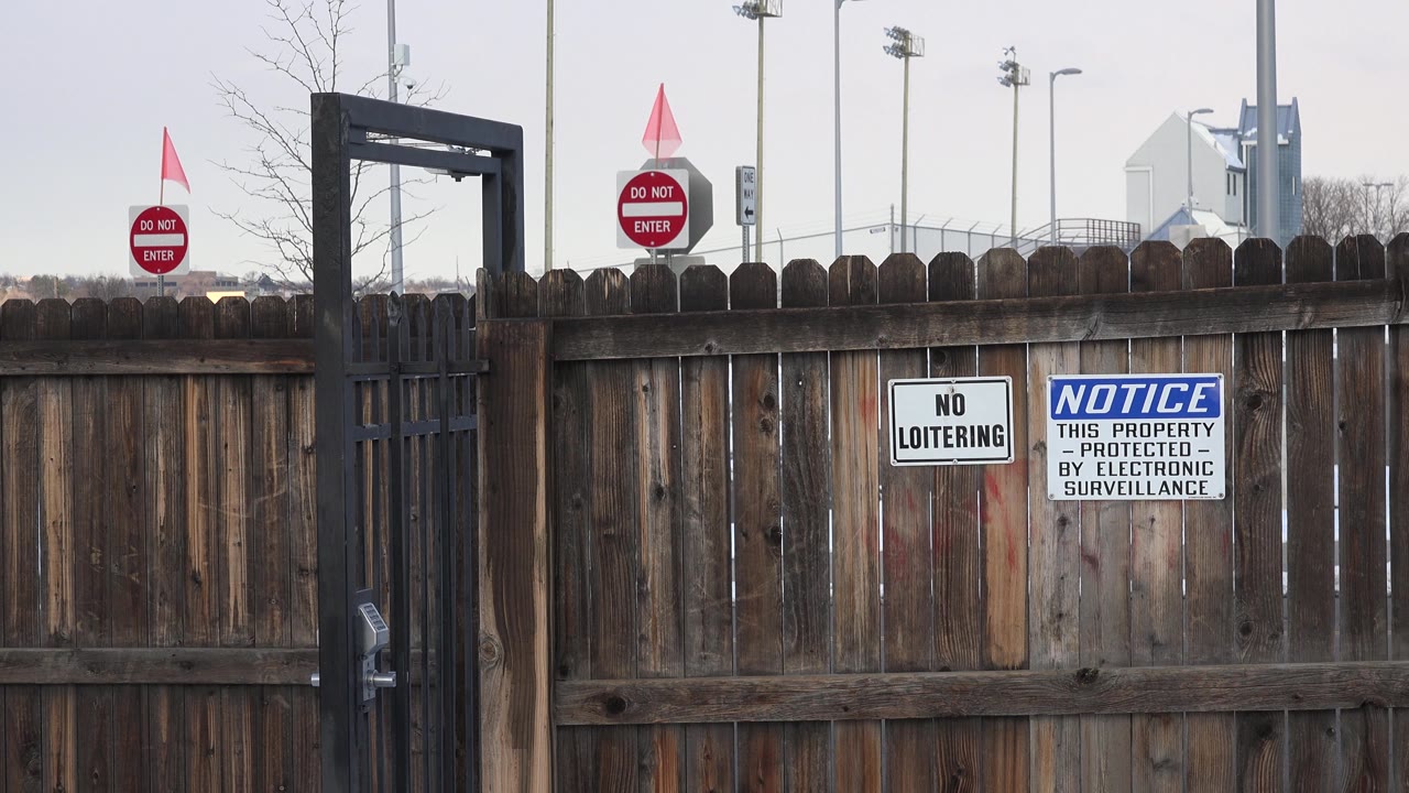 Iron gate beside a wooden fence with snow and warning signs.
