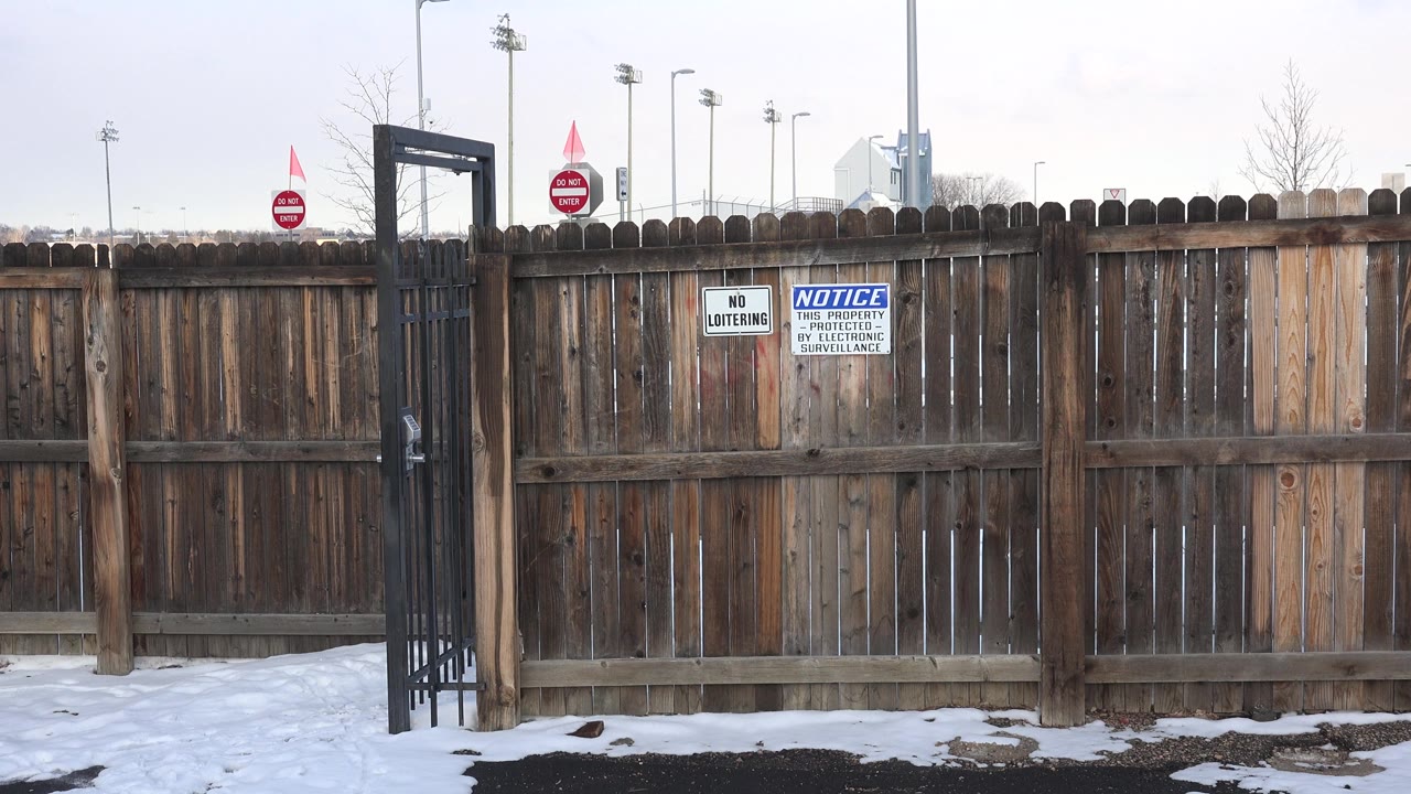 Wooden fence and black gate beside snow-covered ground.