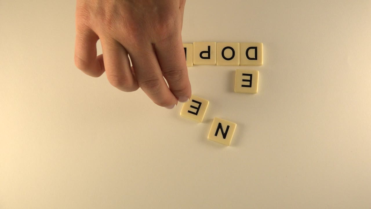 Hand above cream letter tiles on a pale tabletop.