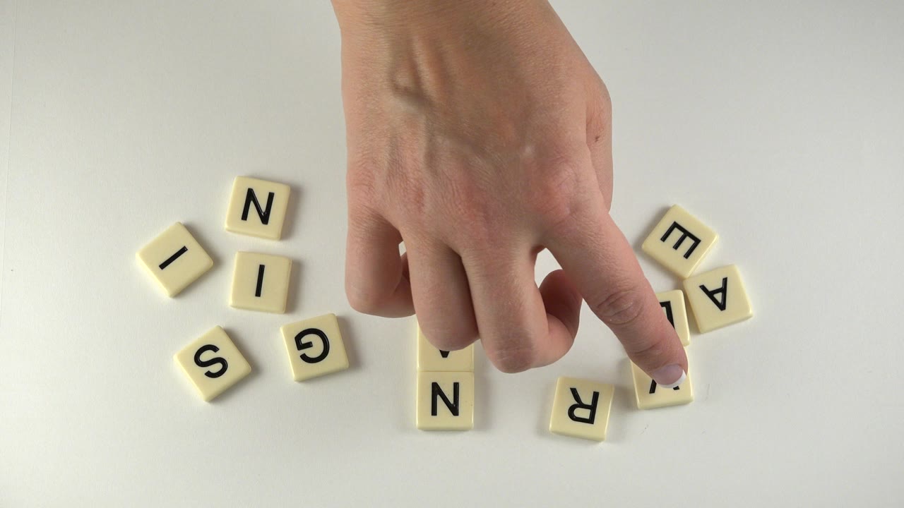 Hand pointing near scattered letter tiles on a white tabletop.