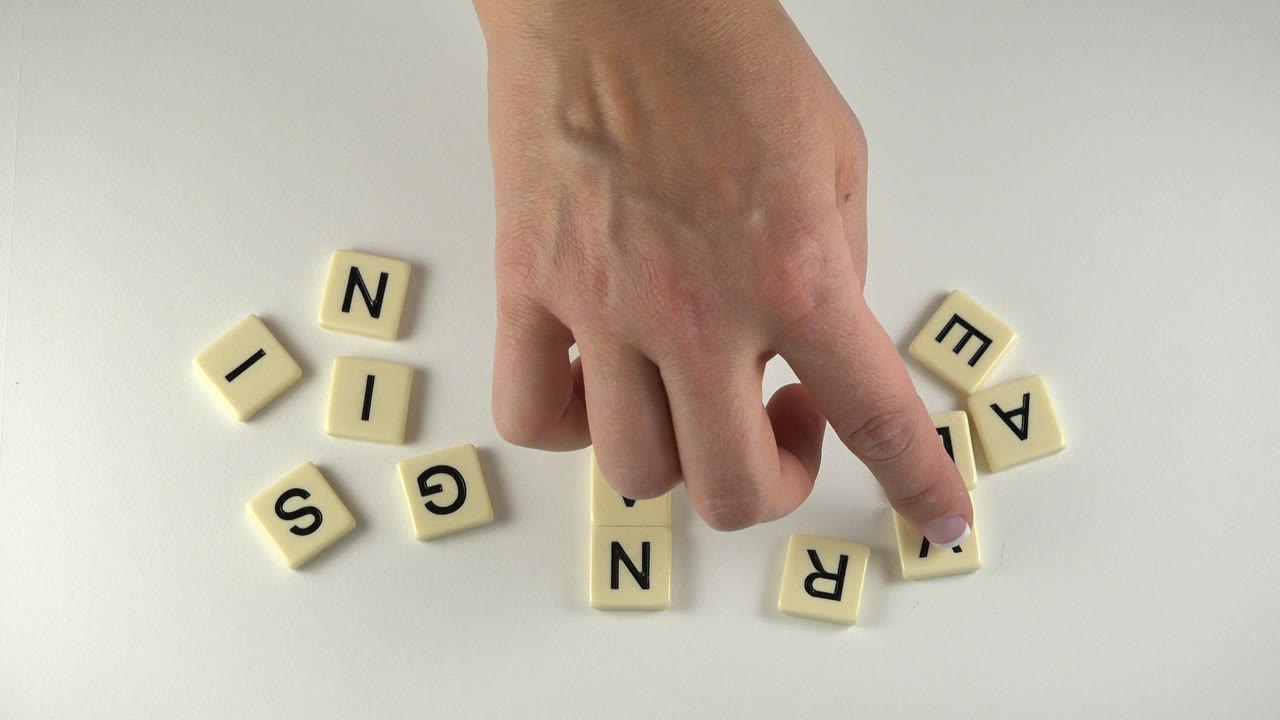 In Westminster, Colorado, the hand presses near a cream letter tile while several black-letter tiles sit loosely grouped on the white surface.