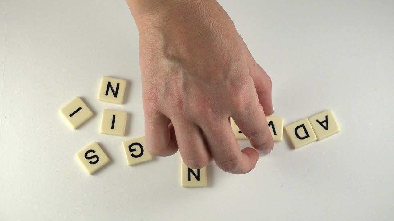 At 0:00 in Westminster, Colorado, a hand reaches down toward cream letter tiles scattered on a pale tabletop, with no face visible.