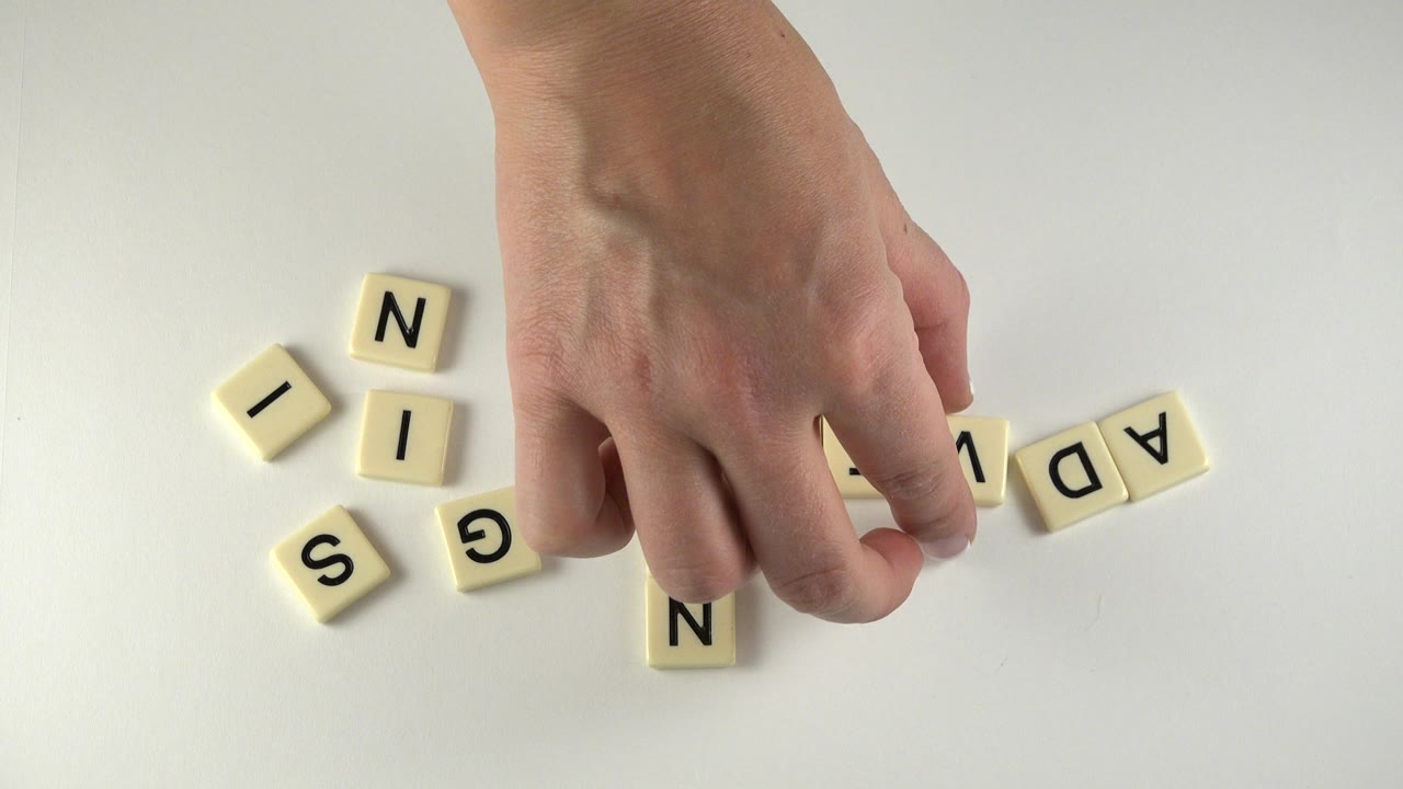 At 0:01 in Westminster, Colorado, the hand hovers over the center of the tabletop as loose SIGN tiles sit to the left and other tiles begin to line up on the right.