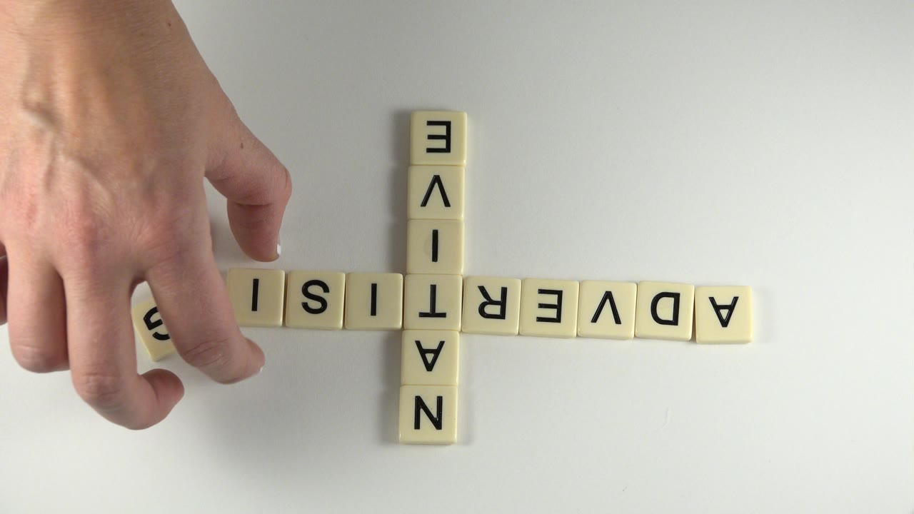 Hand moving a tile at the start of the word ADVERTISING.