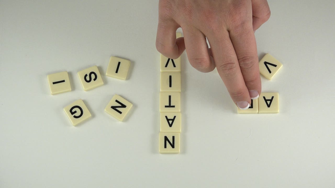 Hand reaching toward letter tiles on a pale tabletop.