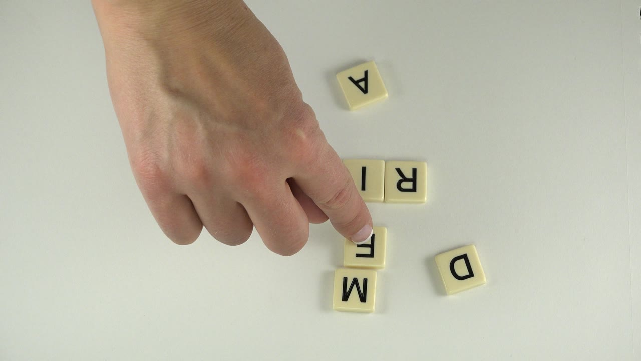 Hand touching letter tiles on a pale tabletop.