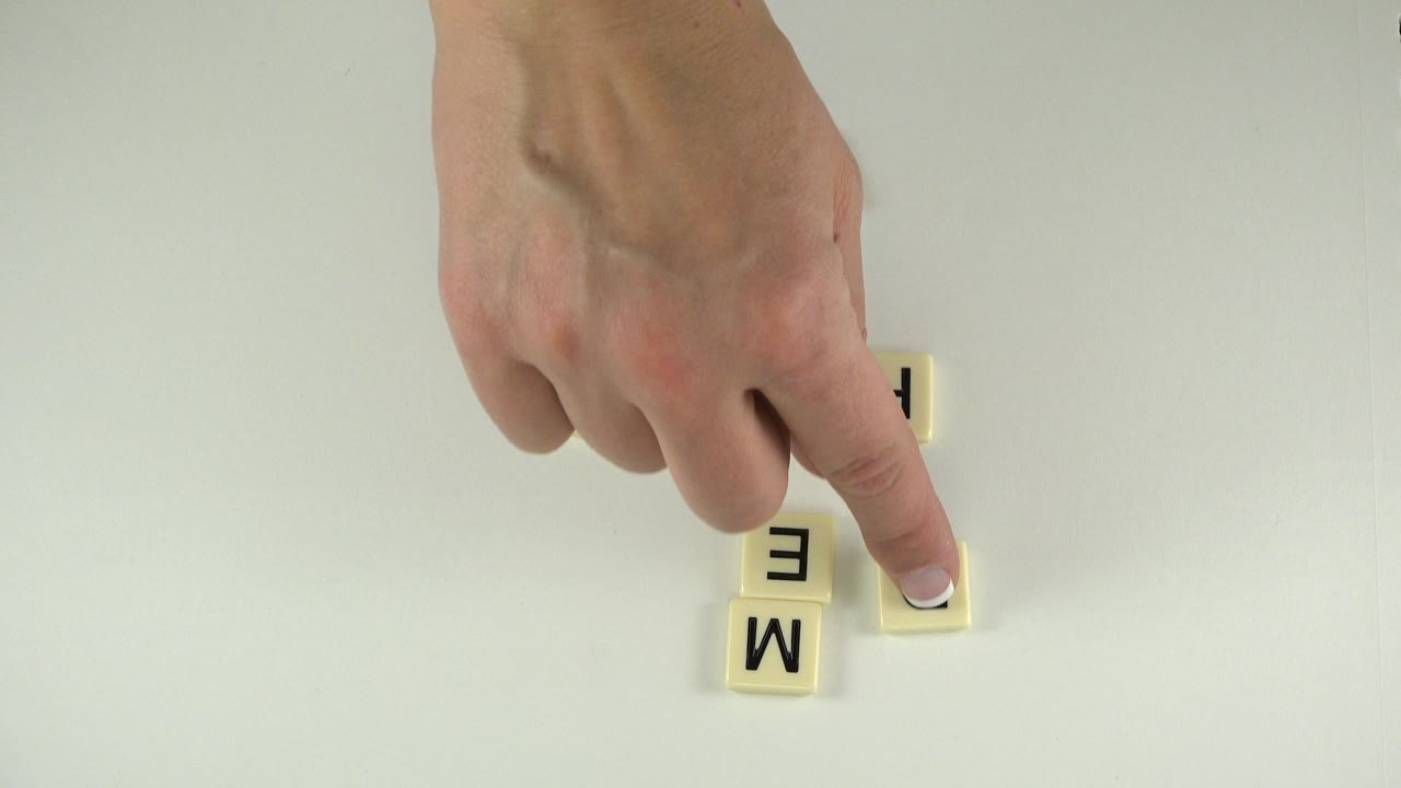 In Westminster, Colorado, the fingertip touches a tile at the right edge of a small cluster, with E and M tiles stacked nearby on the tabletop.
