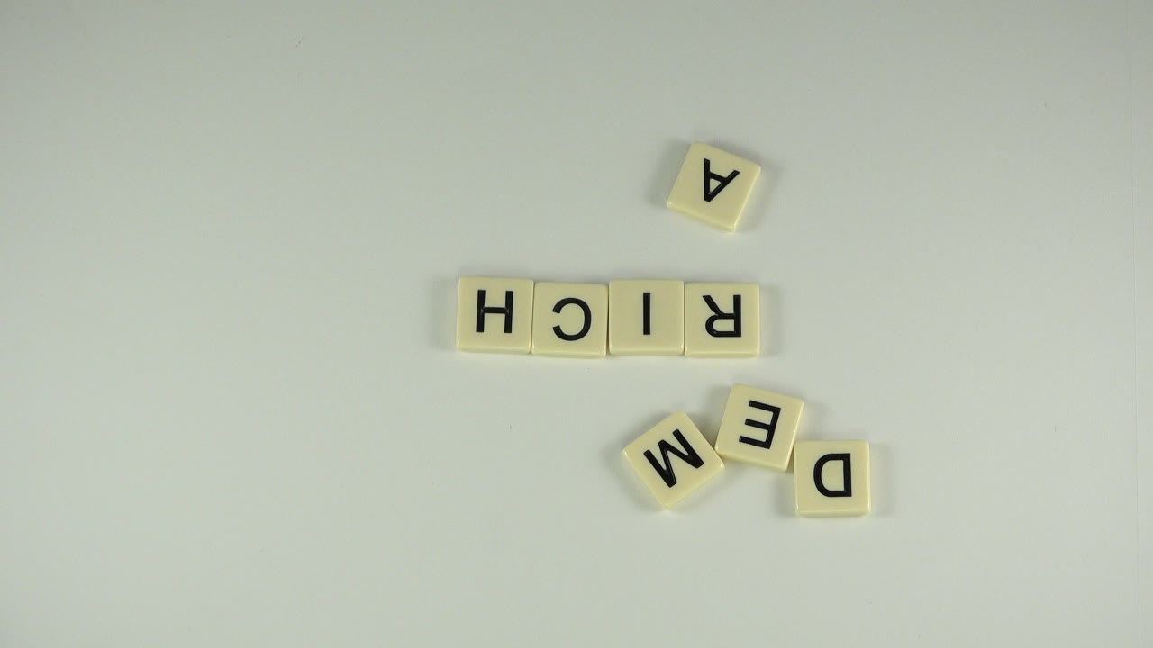 Letter tiles spelling RICH with loose A, M, E, and D tiles on a pale table.