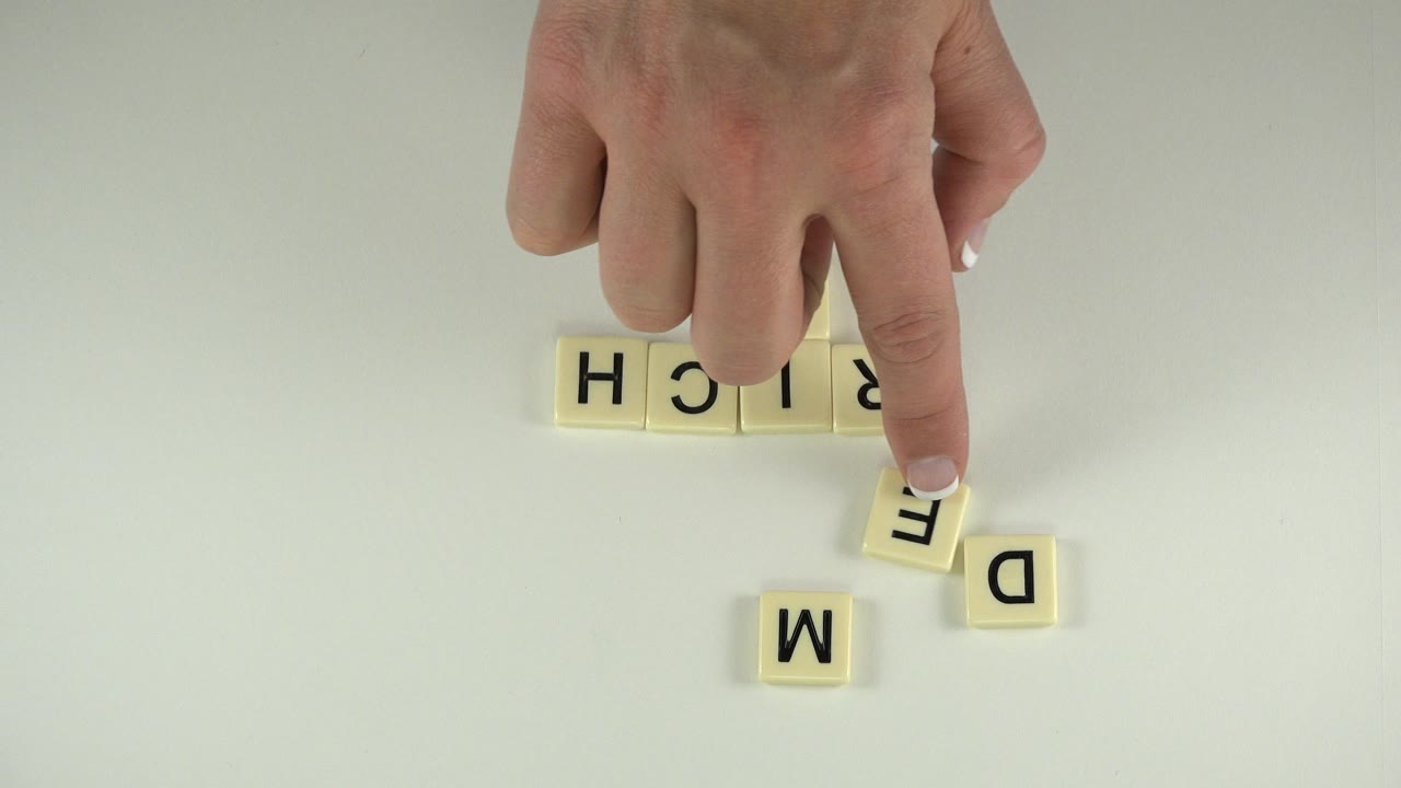 Hand pointing at cream letter tiles on a pale tabletop