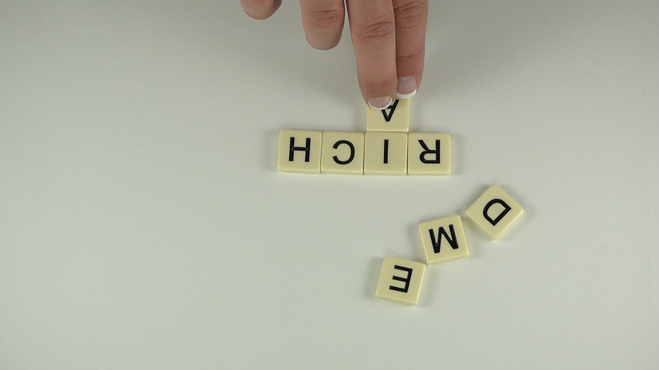 Hand placing a letter tile near tiles spelling RICH