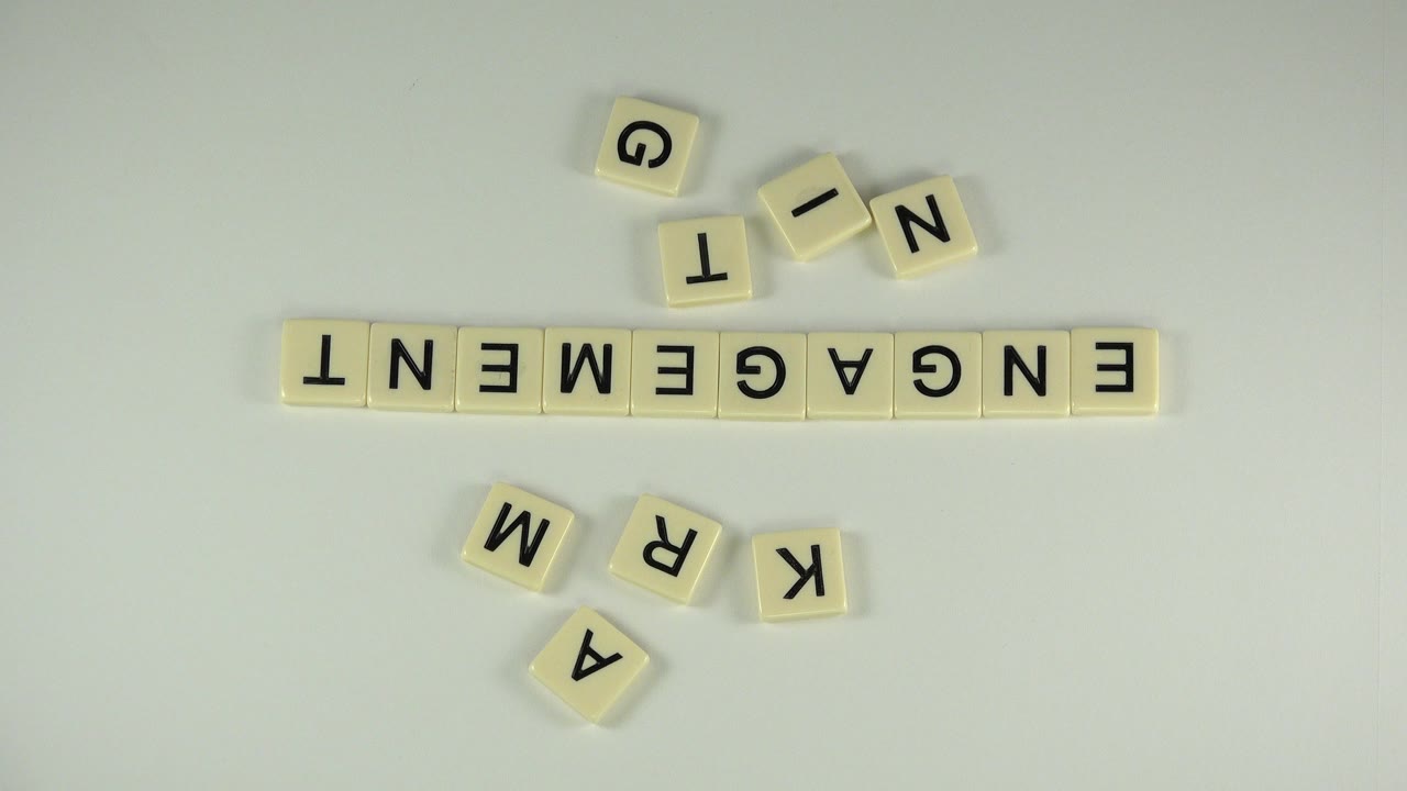 Letter tiles spell ENGAGEMENT on a white table with loose tiles nearby.