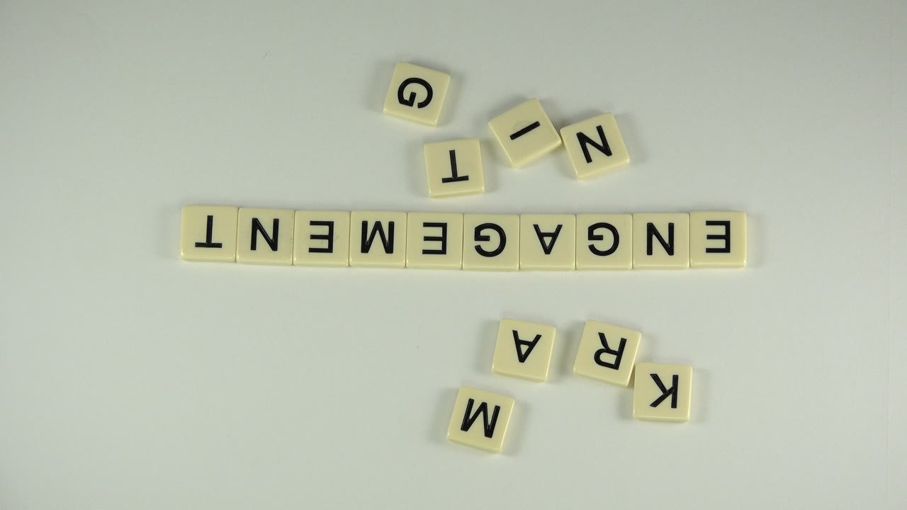 Static overhead frame of the Westminster, Colorado word puzzle showing ENGAGEMENT in a row, with loose G, T, I, N, M, R, A, and K tiles around it and no visible people.