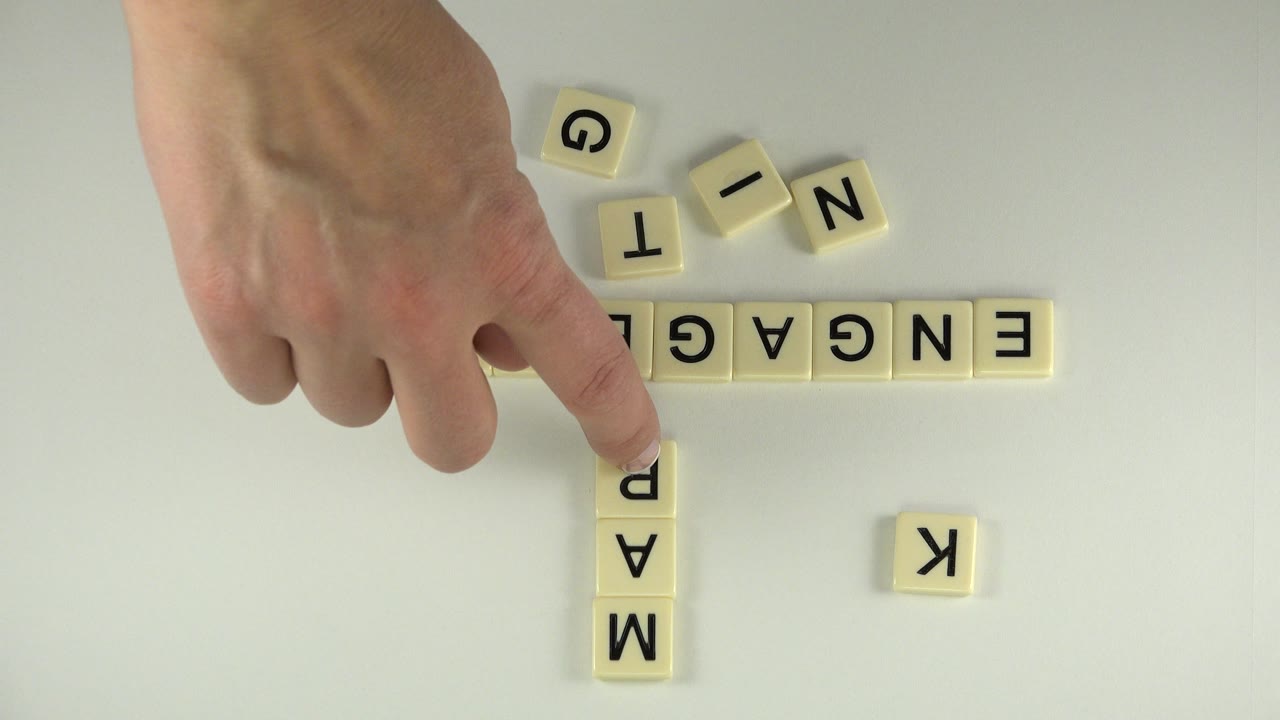 Adult hand points at letter tiles spelling ENGAGEMENT and MARK.