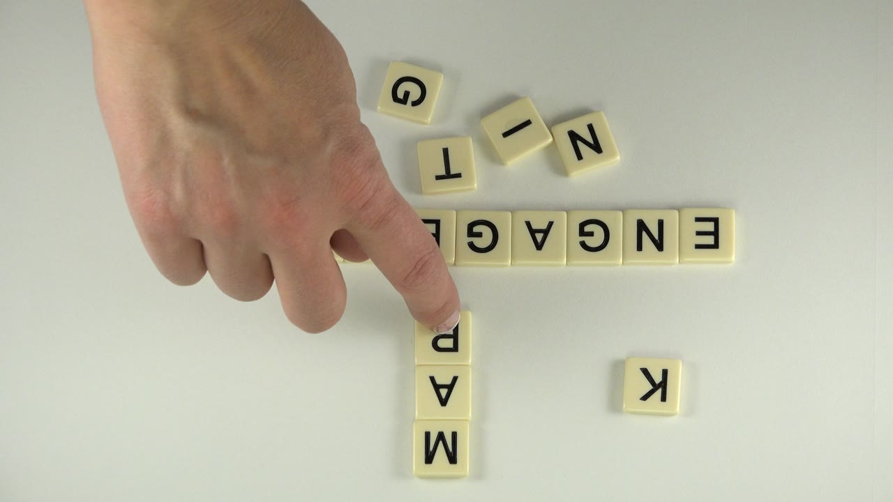 The hand remains over the letter-tile arrangement, with ENGAGEMENT running horizontally and MARK visible below the crossing tile in the Westminster, Colorado clip.